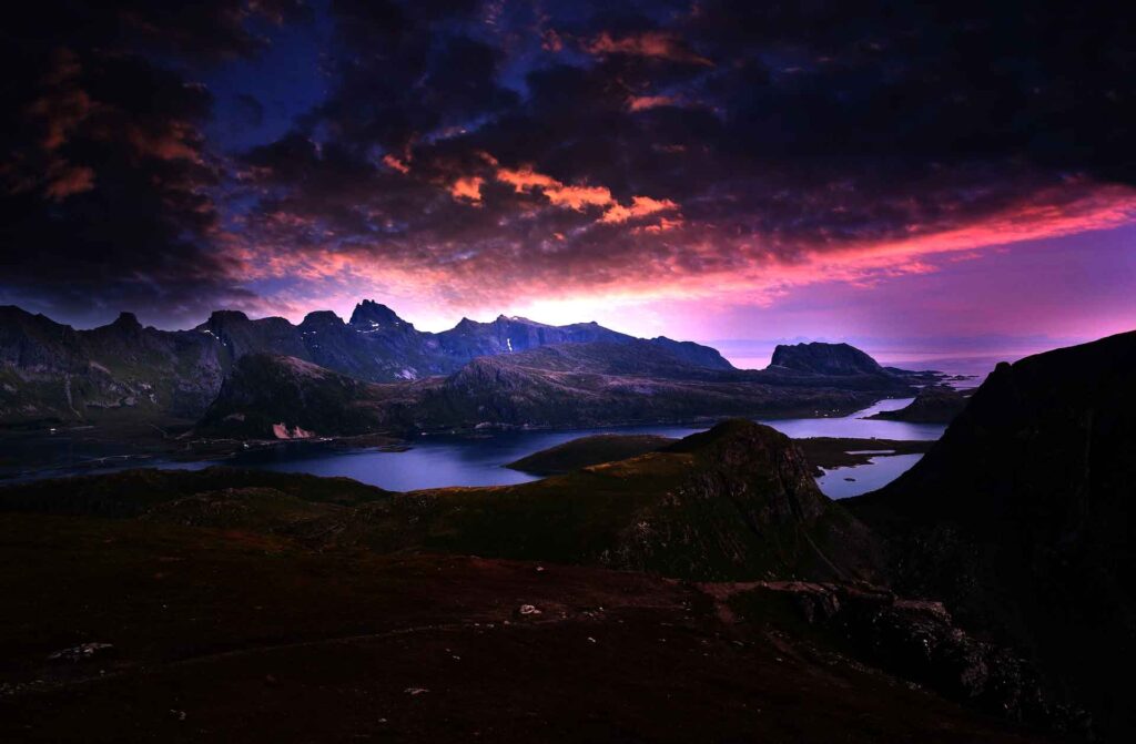 Photo of the sun shining through purple clouds over majestic mountains.