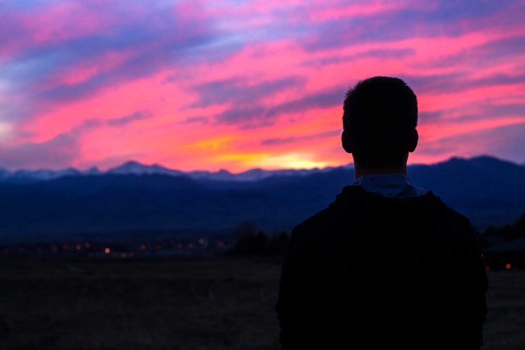 Photo of a man alone looking at the sunset over the mountains.