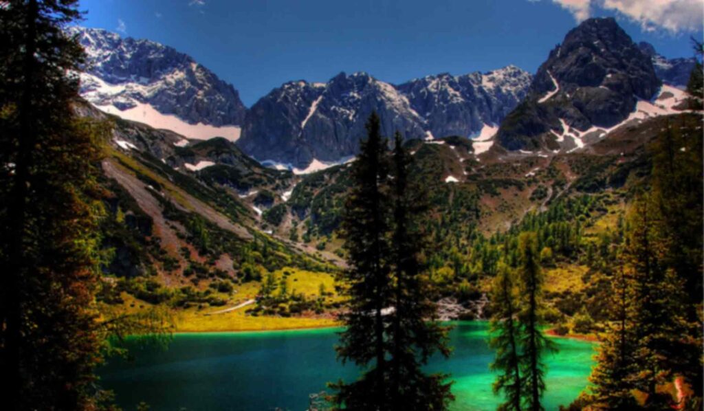 Photo of tranquil snowcapped mountains with a lake and pine trees.